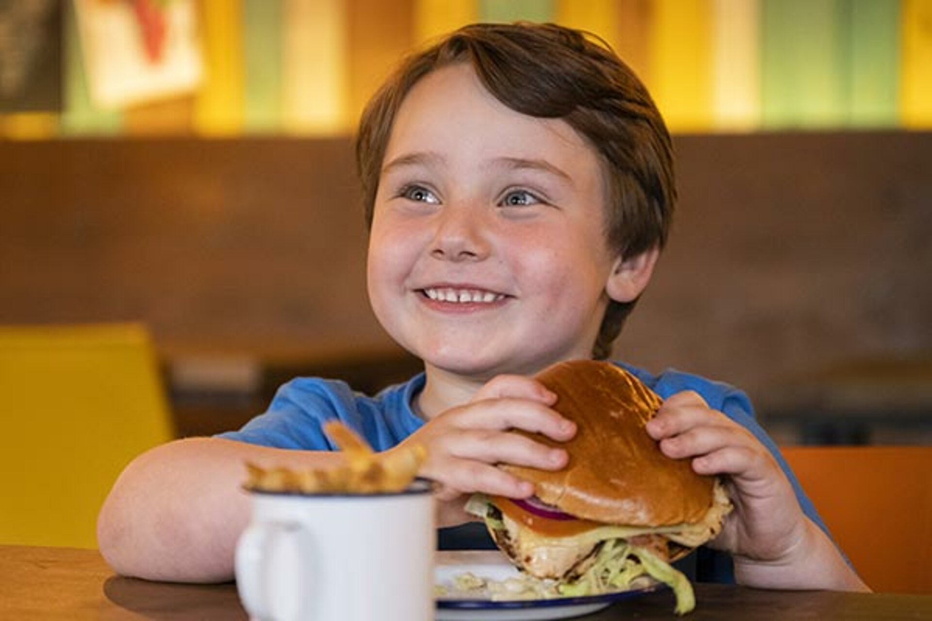 Boy smiling and holding a burger inside the Burger Co at West Midlands Safari Park, enjoying a fun, family-friendly meal experience